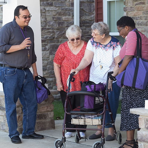 Library employees standing with 2 older ladies one with a walker.